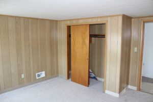 Empty room with wood-paneled walls and an open closet door.