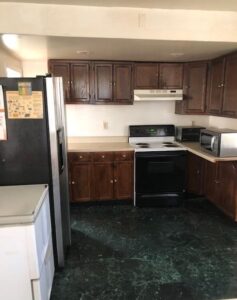 A kitchen with dark wood cabinets, black appliances, and green flooring.