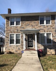 Two-story stone house with a black front door and white window frames.