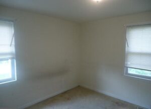 Empty room with beige walls and carpet, a small window with blinds.