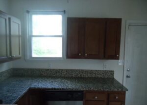 Kitchen countertop with granite surface and wooden cabinets under natural light.