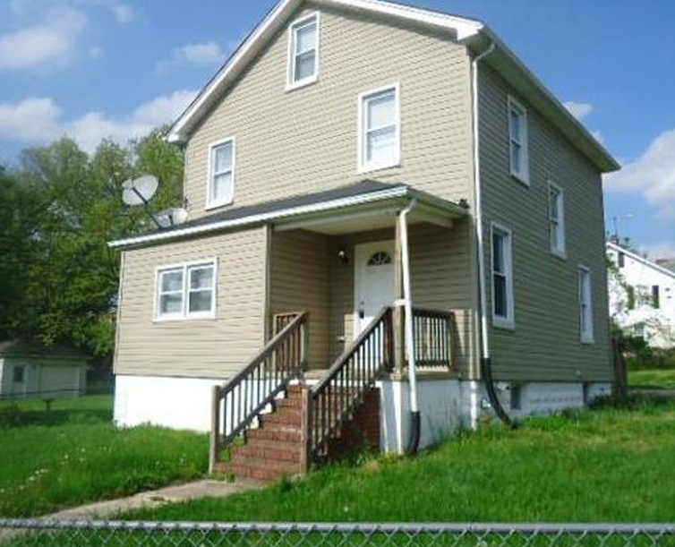 Two-story beige house with front porch and stairs.