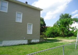 Side view of a beige house with white-trimmed windows and a small fenced yard.